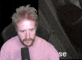 a man in a pink shirt is sitting in front of a microphone and the word se is on the screen