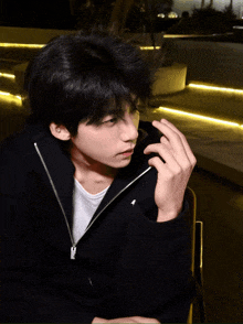 a young man wearing a black jacket and a white shirt has his hand on his chin