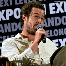 a man speaking into a microphone in front of a sign that says expo ando