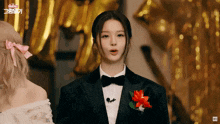 a woman in a tuxedo with a flower on her lapel stands in front of balloons