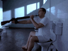 a man sits on a toilet with a gun in his mouth