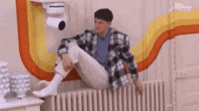 a man in a plaid shirt is sitting on a radiator in front of a colorful wall .