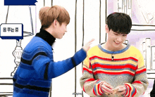 two young men are standing next to each other and one of them is wearing a colorful striped sweater