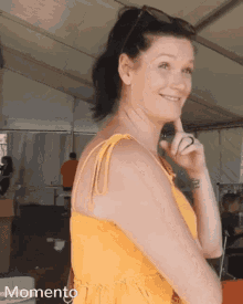 a woman in a yellow dress is smiling in front of a white tent with the word momento on the bottom right