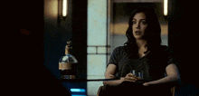 a woman is sitting at a table with a glass of whiskey and a bottle of whiskey in the background .