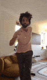 a man with a beard is dancing in a living room next to a couch .