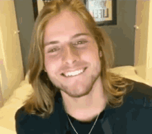a young man with long blonde hair and a beard smiles for the camera