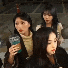 three women are standing next to each other in a parking lot . one of the women is holding a cup of blue liquid .