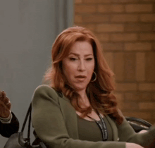 a woman with red hair is wearing a green jacket and a black bag .