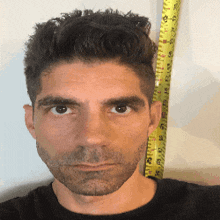 a man in a black shirt is standing next to a yellow measuring tape that goes up to 12 feet