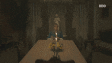 a woman sits at a table with a candle lit and a hbo logo in the background
