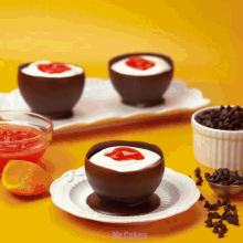 three chocolate bowls filled with whipped cream and strawberry sauce on a white plate