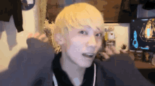 a young man with blonde hair is standing in front of a computer monitor