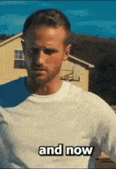 a man in a white shirt is standing in front of a house and says " and now " .
