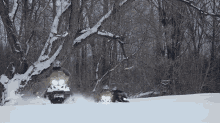 two snowmobiles are driving down a snowy road in the woods