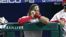 a baseball player wearing a sesame street headband leans against a fence that says transfer on it