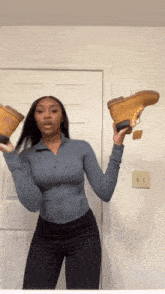 a woman in a blue top is holding a pair of brown boots