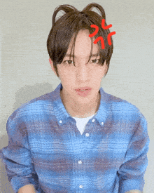 a man in a blue plaid shirt has a red angry face drawn on his hair