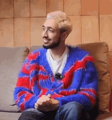 a man is sitting on a couch wearing a red and blue sweater .