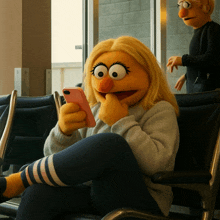 a muppet sitting in a chair looking at a cell phone