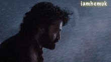 a man with a beard is standing in the rain with the words " iamhemuk " behind him
