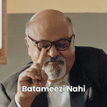 a bald man with glasses and a beard is pointing at his nose and the caption batameezi nahi