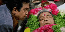 two men are looking at a man laying in a coffin with flowers around it