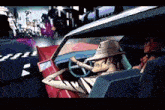 a man in a hat is driving a red car