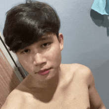 a shirtless young man taking a selfie with a blue towel in the background