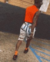 a man wearing ripped shorts and an orange shirt stands in a handicapped parking space