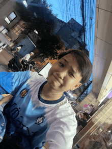 a young boy wearing a blue and white shirt with the letter l on it takes a selfie