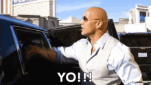 a bald man wearing sunglasses is standing next to a car and says yo