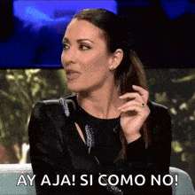 a woman in a black dress is sitting on a couch and saying ay aja ! si como no !