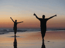 a man and a woman standing on a beach with their arms outstretched