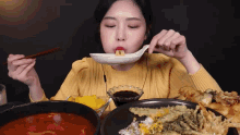 a woman in a yellow sweater is eating a meal with chopsticks