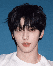 a young man with black hair and a white shirt looks at the camera