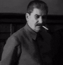 a man with a mustache is smoking a cigarette and making a hand gesture in a black and white photo .