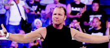 a wrestler is standing in front of a crowd with his arms outstretched and giving a thumbs up .