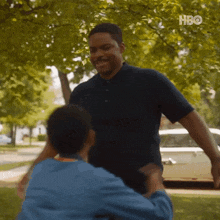 a man in a blue shirt is hugging another man in a wheelchair in a park .