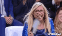 a woman wearing glasses and a blue dress is laughing while holding a smoke bomb .