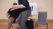 a man in an adidas hat stands next to another man in a chair