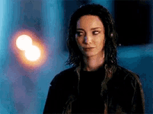a woman in a black jacket is standing in a dark room looking at the camera .