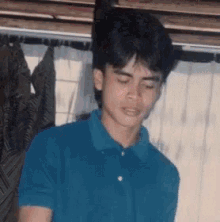a young man wearing a blue polo shirt is standing in front of a window .