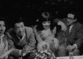 a group of people sitting around a table with glasses of water and flowers