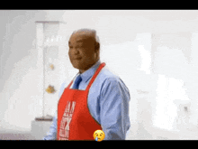 a man wearing a red apron and a blue shirt is standing in a kitchen .
