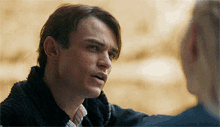 a man in a black sweater talks to another man in a blue suit