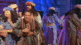 a group of people in costume are dancing on a stage in front of a blue light .