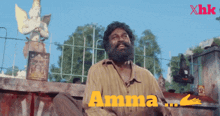 a man with a beard is sitting in front of a fence and the word amma is on the screen