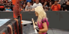 a woman is standing in a wrestling ring holding a rope while a crowd watches .