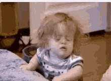 a baby is sitting on a couch with his eyes closed and his hair blowing in the wind .